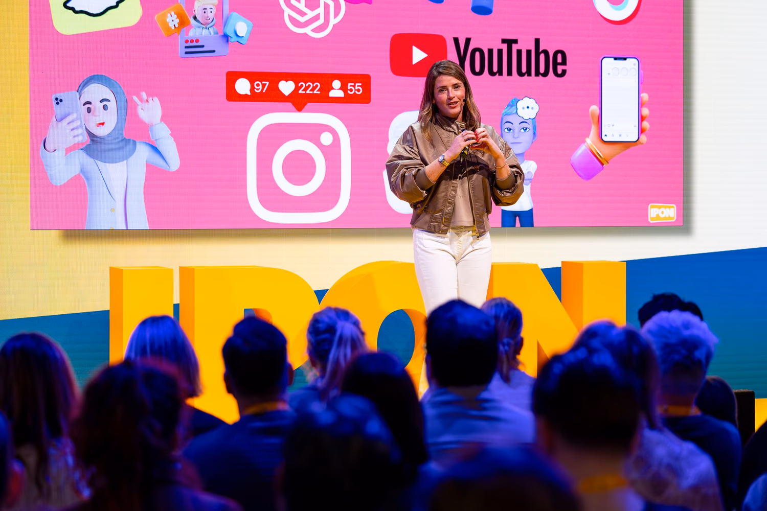 Stephanie op het podium van IPON met social media beelden op het scherm